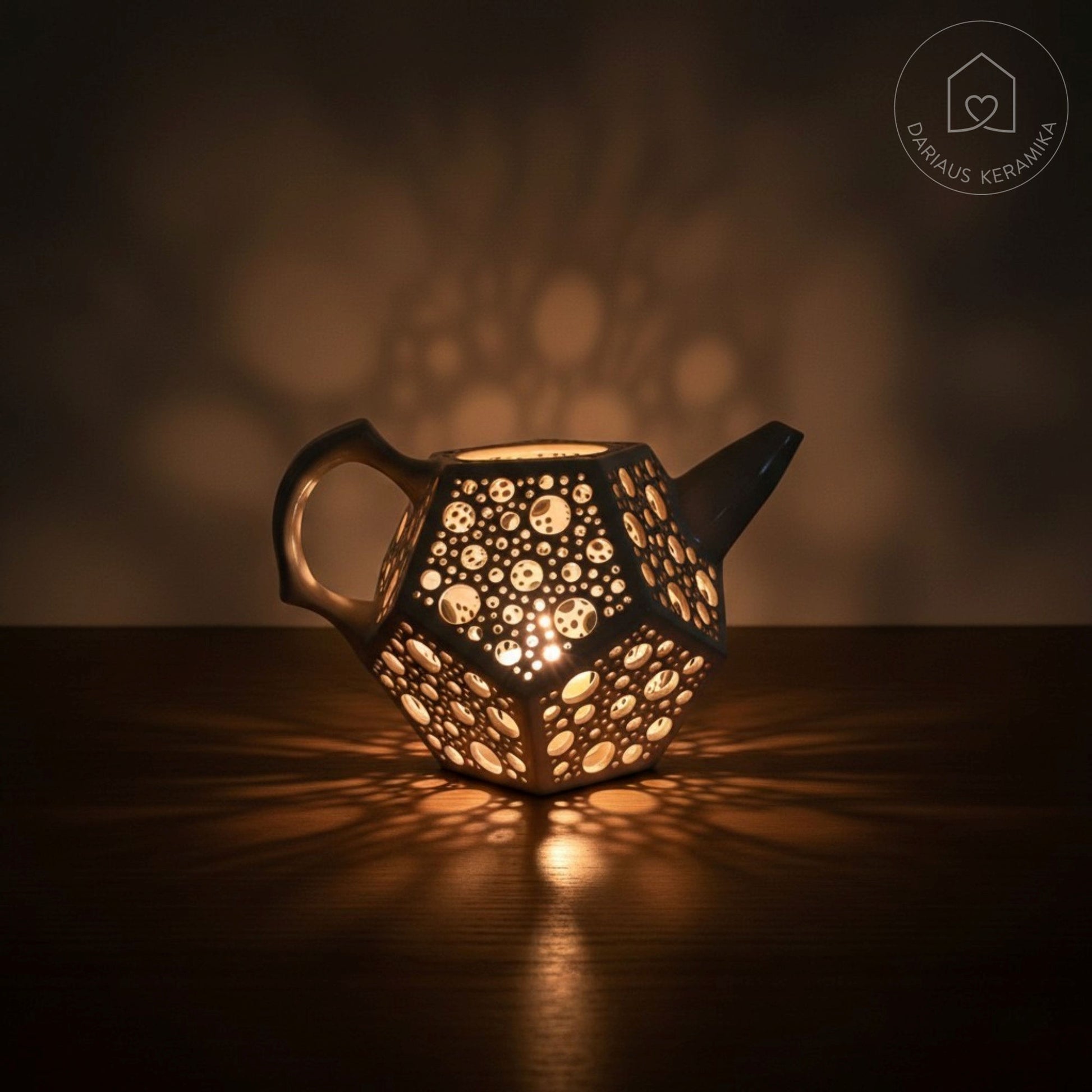 Ažūrinė balta keraminė žvakidė arbatinukas dodekaedro formos skleidžianti šviesą tamsoje ant medinio stalo