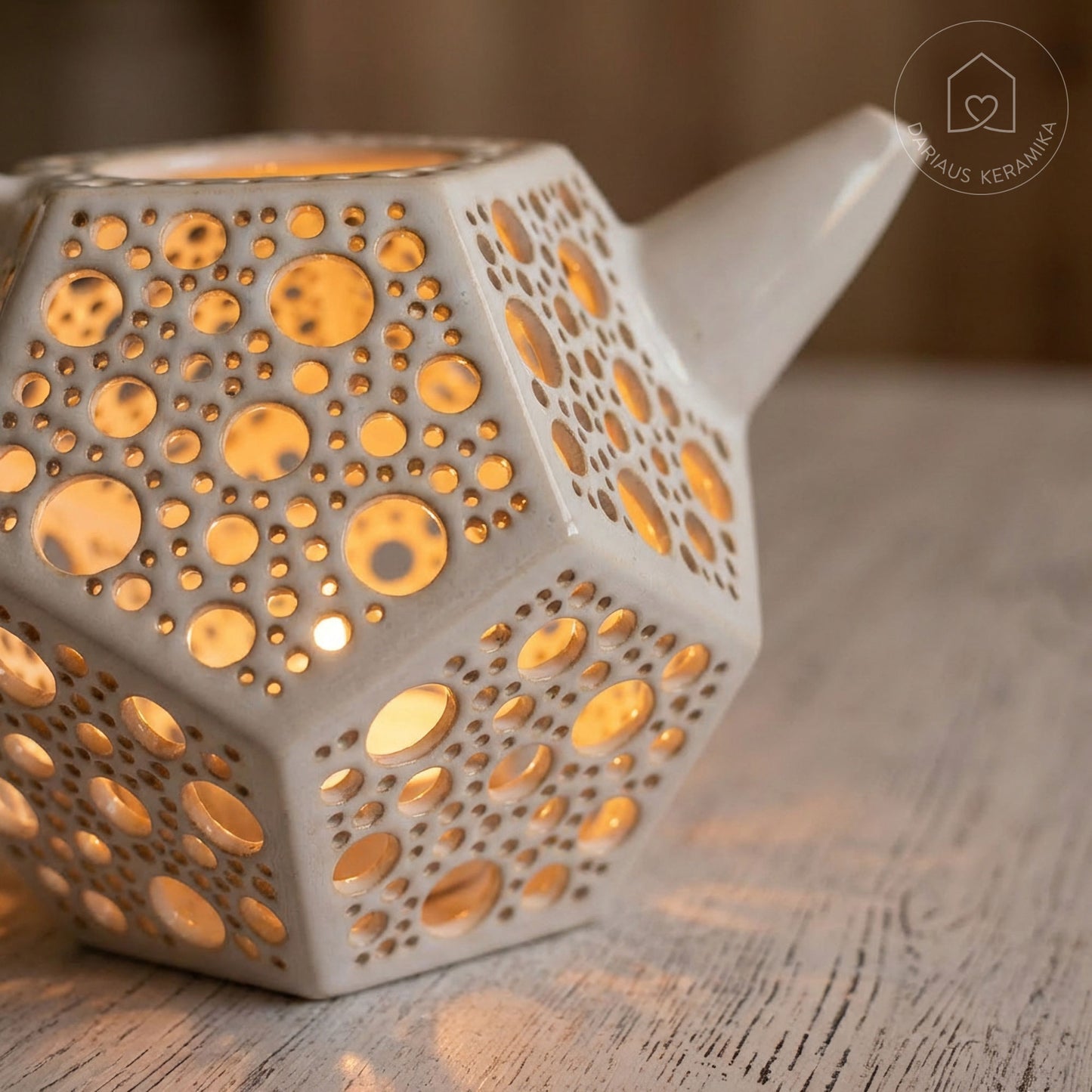 Ažūrinė balta keraminė žvakidė arbatinukas dodekaedro formos skleidžianti šviesą tamsoje ant medinio stalo